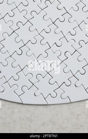 Un puzzle blanc de forme complète repose sur une surface en pierre traitée. Image texturée avec espace de copie