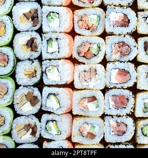 Gros plan d'un grand nombre de petits pains à sushis avec différentes garnitures. Photo macro de plats japonais classiques cuits. Image d'arrière-plan Banque D'Images