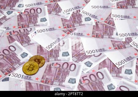 Bitcoins sur un tas de cinq cents billets en euros. Concept de monnaie traditionnelle versus crypto-monnaie. Pièce d'or au-dessus de 500 euros de factures. Gros plan Banque D'Images