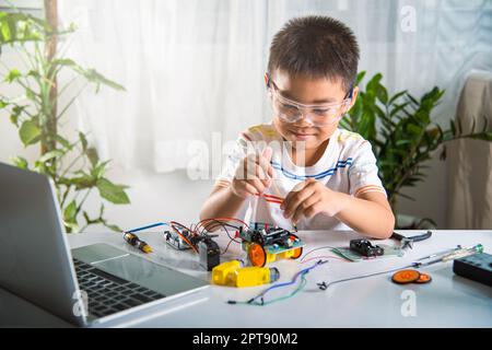 Petit garçon asiatique assemblant le projet de devoirs de voiture robot Arduino à la maison, petit enfant serrer l'écrou à l'aide d'un tournevis pour assembler le jouet de voiture, en créant Banque D'Images