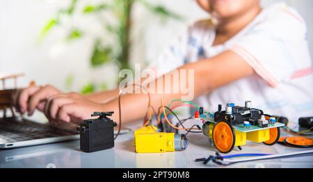 Un jeune garçon asiatique apprend le codage et la programmation avec un ordinateur portable pour la voiture robot Arduino, les jeunes élèves tapant le code dans l'ordinateur en ligne avec le jouet de voiture, STEA Banque D'Images