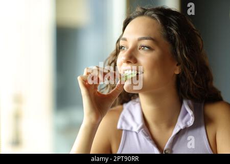 Bonne femme mangeant du kiwi à la maison en regardant par une fenêtre Banque D'Images