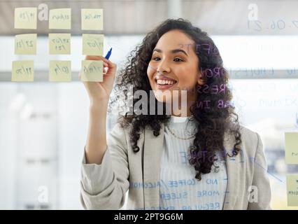 La planification est la clé pour réaliser vos rêves. une jeune femme d'affaires remue-méninges avec des notes sur un écran de verre dans un bureau Banque D'Images