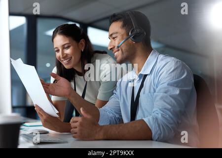 Doublez la compétence, doublez la récompense. un jeune homme et une jeune femme lisant un document tout en travaillant dans un centre d'appels Banque D'Images