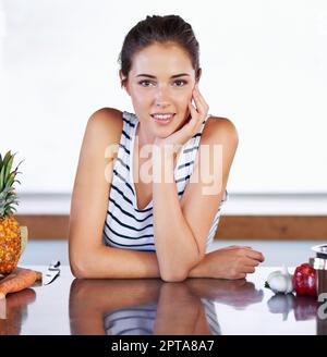 Je suis confiant dans mes choix sains. Un portrait d'une belle jeune femme s'appuyant sur son comptoir de cuisine à côté de la nourriture et d'un pot de cuisine Banque D'Images