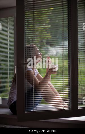 Femme d'âge moyen qui allume une cigarette à la maison, obtient sa dose quotidienne de nicotine, incapable de résister à son habitude malsaine Banque D'Images