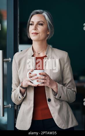 Les bonnes idées commencent par le café. une femme d'affaires attirante et mûre debout seule et appréciant une tasse de café dans son bureau à la maison Banque D'Images