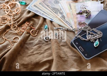 Lot de bijoux volés, d'argent et de smartphones sur tissu militaire uniforme. Pillage par des soldats russes dans les villes ukrainiennes pendant la Russie Banque D'Images