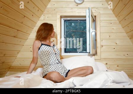 La femme endormi s'assoit dans le lit et regarde dans la fenêtre ouverte Banque D'Images