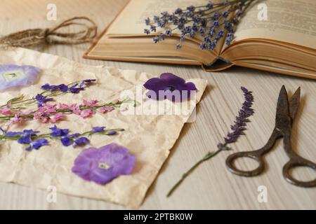 Belles fleurs séchées, livre et ciseaux sur table en bois, gros plan Banque D'Images