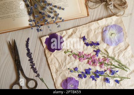 Composition de plat avec de belles fleurs séchées, livre et ciseaux sur table en bois Banque D'Images