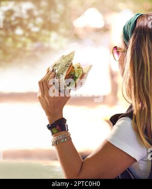 Il est temps de goûter un peu. une jeune femme mangeant un hamburger dehors Banque D'Images