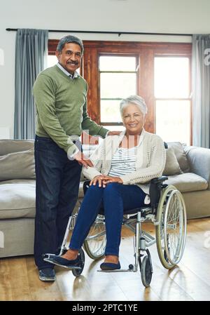 Rien ne va nous faire retomber. Portrait d'une jeune femme âgée assise dans un fauteuil roulant tout en étant soutenue et tenue par son mari à l'intérieur de Banque D'Images