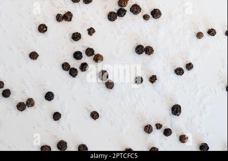 Gros plan du sel de table et des grains de poivre noir dispersés sur un fond blanc Banque D'Images