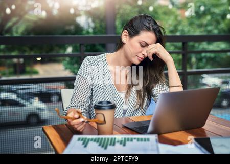 Ces heures supplémentaires lui sont vraiment d'arriver. une jeune femme d'affaires attirante qui a l'air stressée en travaillant sur son ordinateur portable dans un café Banque D'Images