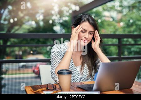 Le stress est une sous-affirmation. une jeune femme d'affaires attirante qui a l'air stressée en travaillant sur son ordinateur portable dans un café Banque D'Images