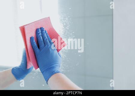 Vue rognée de la femme de ménage main en caoutchouc bleu gant polissage, nettoyage, miroir glissant avec chiffon, pulvérisation de liquide nettoyant pendant le nettoyage Banque D'Images