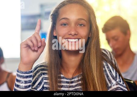 Shes a une question à laquelle il faut répondre. Portrait d'une écolière enthousiaste levant la main pour répondre à une question en classe Banque D'Images