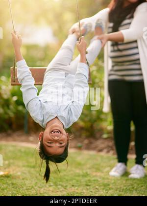 Rotation rapide, rotation lente. Portrait d'une petite fille jouant sur une balançoire à l'extérieur avec sa mère en arrière-plan Banque D'Images