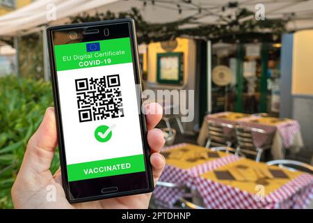 Femme montrant sur smartphone eu Digital Covid certificat Green Pass avec code quadruple. Arrière-plan du restaurant. Banque D'Images