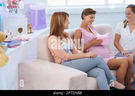 Je me sens si béni aujourd'hui. Une jeune femme enceinte recevant des vêtements de bébé de ses jolies amies à la douche de bébé Banque D'Images