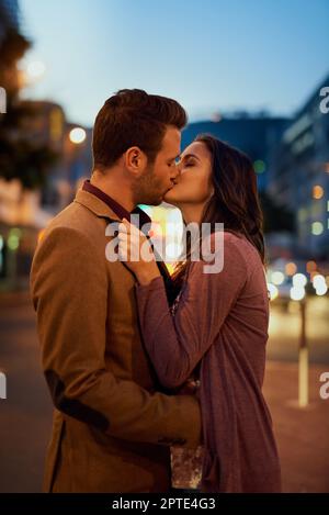 Tomber fou, profondément et vraiment dans l'amour. un jeune couple affectueux partage un baiser dehors la nuit Banque D'Images