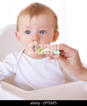 Essayons. Un bébé mignon recevant une cuillerée de nourriture de sa mère Banque D'Images