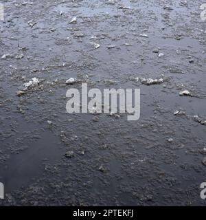 Route asphaltée endommagée avec cassis, remplie d'eau avec de la glace, causée par le gel et la fonte en hiver. Mauvaise route Banque D'Images