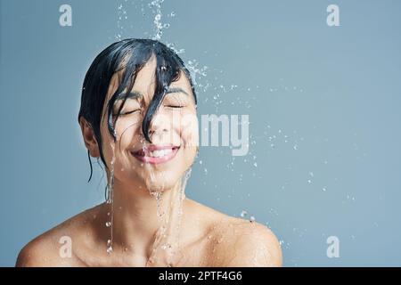 Réveillez ses sens avec une douche rafraîchissante. une jeune femme ayant une douche rafraîchissante sur fond bleu Banque D'Images