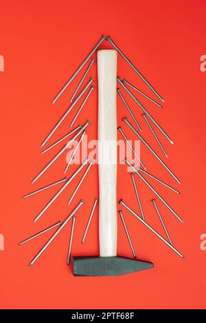 Ongles longs et marteau, disposés en forme d'arbre de Noël sur fond rouge.Vertical, plat Banque D'Images