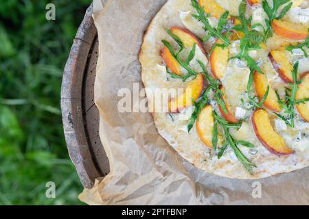 Pizza très savoureuse et intéressante à la pêche et au bleu de la botte avec arugula sur parchemin. Délicieux, goût intéressant de pizza aux fruits. Pizza grillée, outdoo Banque D'Images