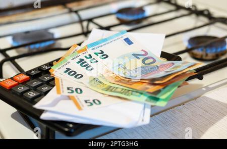 Paiement des factures de services publics, calculs sur une calculatrice. Les billets d'euro et de dollar sont près d'un brûleur à gaz en feu. Le concept d'augmenter le coût de nat Banque D'Images