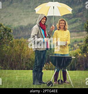 La pluie n'arrêtera pas notre barbecue. un couple se fait un plaisir de faire un barbecue sous la pluie Banque D'Images