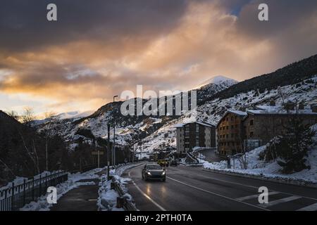 Voitures sur la route menant au village d'El Tarter après la tombée de la nuit. Coucher de soleil avec lumière du soleil éclairant les sommets des Pyrénées, Grandvalira, Andorre Banque D'Images