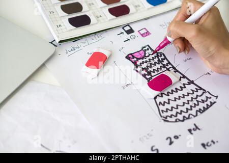 Gros plan mode designer main utiliser Magic stylo peinture sur le motif pour le tissu. Des échantillons de tissus aux couleurs vives sont disponibles sur l'établi. Banque D'Images