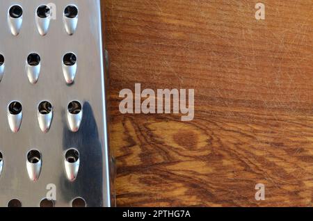 La râpe chromée repose sur la planche à découper avec beaucoup de cicatrices de la hache et du couteau. Image d'arrière-plan pour les recettes de cuisine Banque D'Images