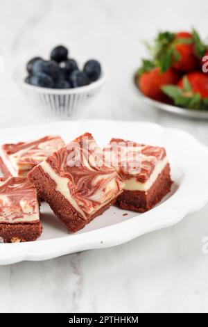 Brownies au fromage à la crème de velours rouge sur une assiette en céramique blanche. Pâte rouge cuite avec garniture de marbre au fromage crème Brownie Banque D'Images