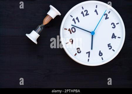 Horloge blanche et sablier sur fond en bois noir. Vue de dessus. Copier l'espace. Concept d'éducation ou d'entreprise. Banque D'Images