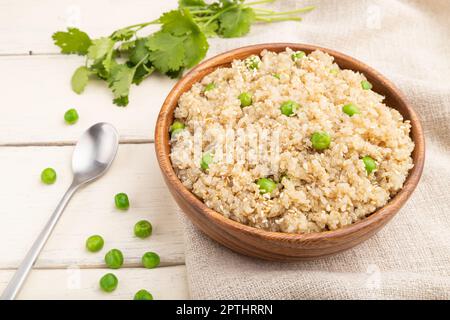 Bouillie de quinoa aux pois verts dans un bol en bois sur fond blanc en bois et linge de maison. Vue latérale, gros plan. Banque D'Images