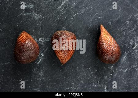 Trois fruits frais Salak ou Salaca zalacca sur table en marbre noir, fruits exotiques Banque D'Images