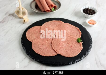 Tranches de saucisse fumées, saucisse finement coupée, prêtes à cuire. Salami de bœuf sur l'assiette noire Banque D'Images