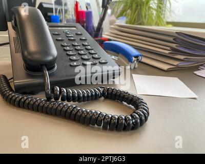 téléphone filaire noir sur le bureau à côté d'un ordinateur portable dans le bureau. Banque D'Images