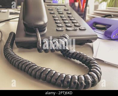 téléphone fixe au bureau sur la table. combiné noir avec boutons et écran. moyens de communication au bureau. fil noir sur tube. Banque D'Images