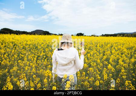 Belle fille aux cheveux blone pose au milieu d'un champ de fleurs de colza jaune Banque D'Images