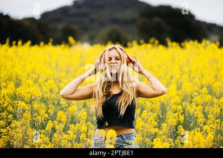 Belle fille aux cheveux blone pose au milieu d'un champ de fleurs de colza jaune Banque D'Images