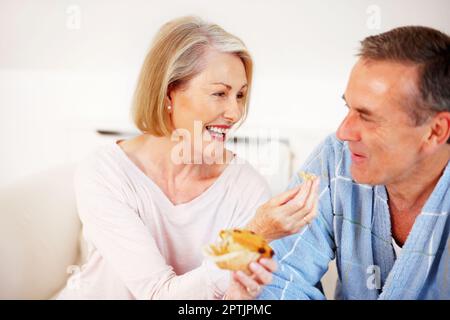 Bonne humeur femme mûre nourrissant un muffin à son mari. Portrait d'une femme mûre et gaie qui nourrit son mari de muffin Banque D'Images