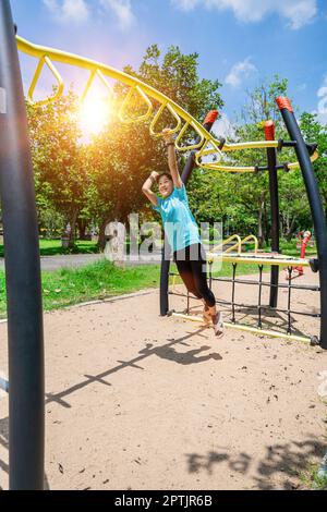 Une petite fille adorable qui pendait sur des barres de singes à l'aire de jeux du parc à l'extérieur. Petite fille mignonne s'amuser dans le jardin d'été. Banque D'Images