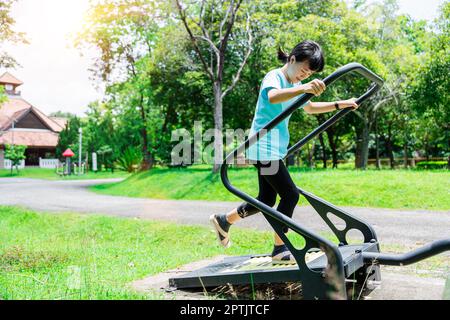 Gros plan d'une fillette qui court sur un tapis roulant pour faire de l'exercice sur le terrain de jeu dans le parc extérieur. Concept de forme physique et de mode de vie sain Banque D'Images