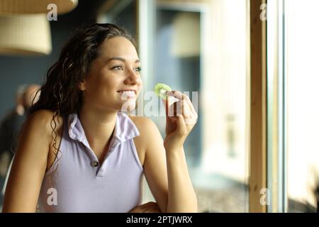 Une femme heureuse dans un restaurant mangeant du kiwi en regardant loin par une fenêtre Banque D'Images