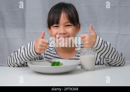 Jolie fille asiatique buvant un verre de lait le matin avant d'aller à l'école. La petite fille mange des légumes sains et du lait pour ses repas. Santé FO Banque D'Images